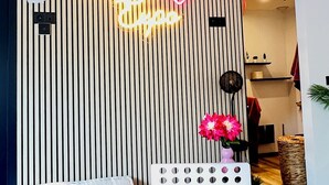 Een moderne woonkamer met een lambrisering, een neonbord, een gezellige bank, een kleine tafel met een vaas en een mand.