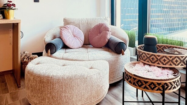 Een moderne woonkamer met een bank en voetenbankje, een salontafel en decoratieve wandplanken.