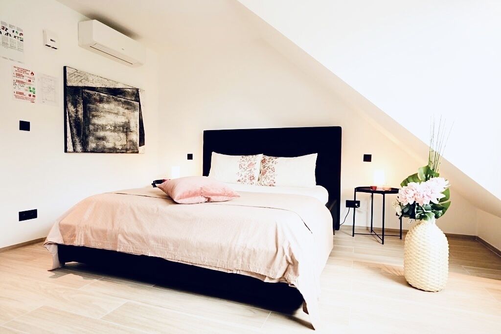 A bedroom with a bed, a nightstand, a vase with flowers, and a wall-mounted air conditioner.