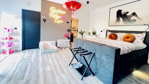 Een moderne slaapkamer met een bed, een bureau en een stoel. Er hangt een neonbord aan de muur en een schilderij.