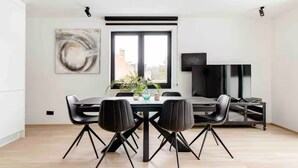 Een moderne eethoek met een grote tafel en stoelen, een potplant en een televisie op een standaard.