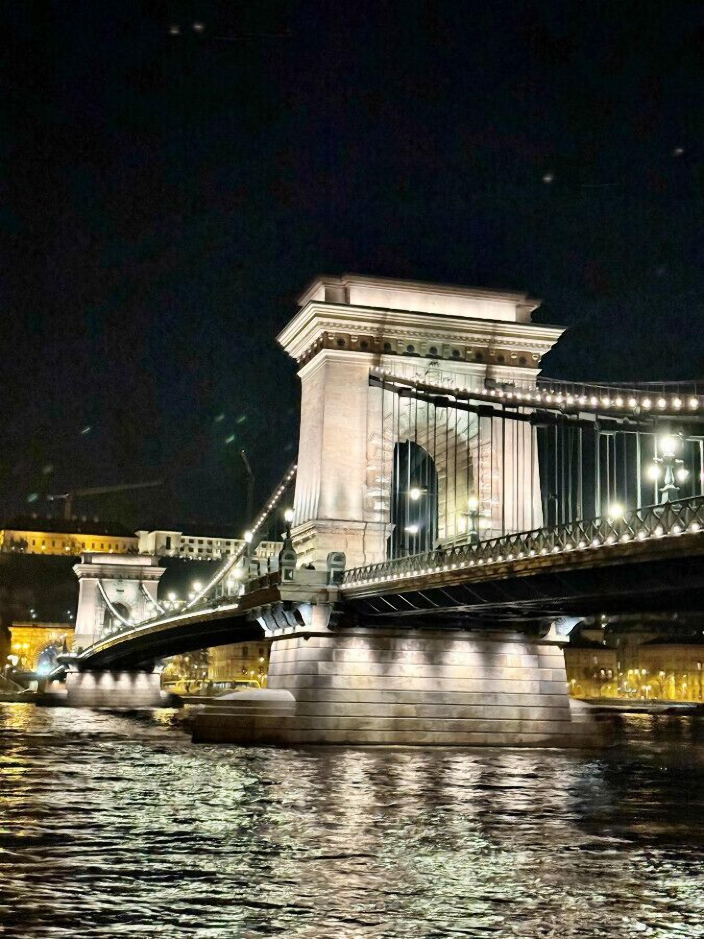 A nighttime view of a bridge with a central tower and illuminated railings.