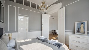 Una camera da letto con un letto grande, un lampadario, una cassettiera bianca e un quadro appeso al muro.