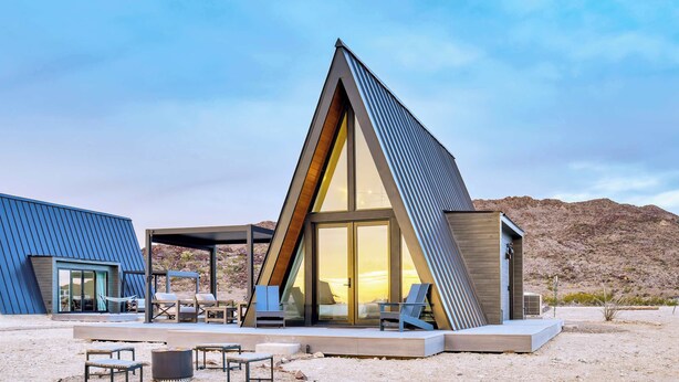 A modern, triangular-shaped building with large glass windows, outdoor seating, and a desert landscape in the background. - Stardust Big Bend Luxury A-Frame#9 with a fab view (Terlingua)