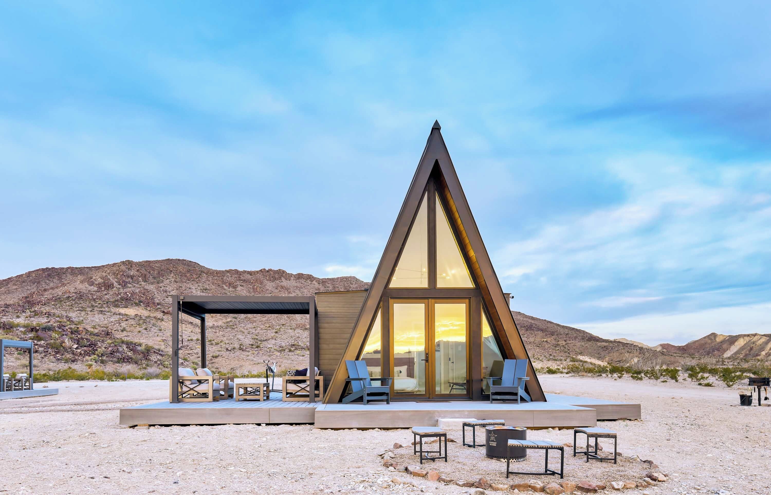 Un bâtiment moderne de forme triangulaire, doté d’une façade en verre, d’un espace extérieur aménagé pour s’asseoir et d’un paysage désertique en arrière-plan.