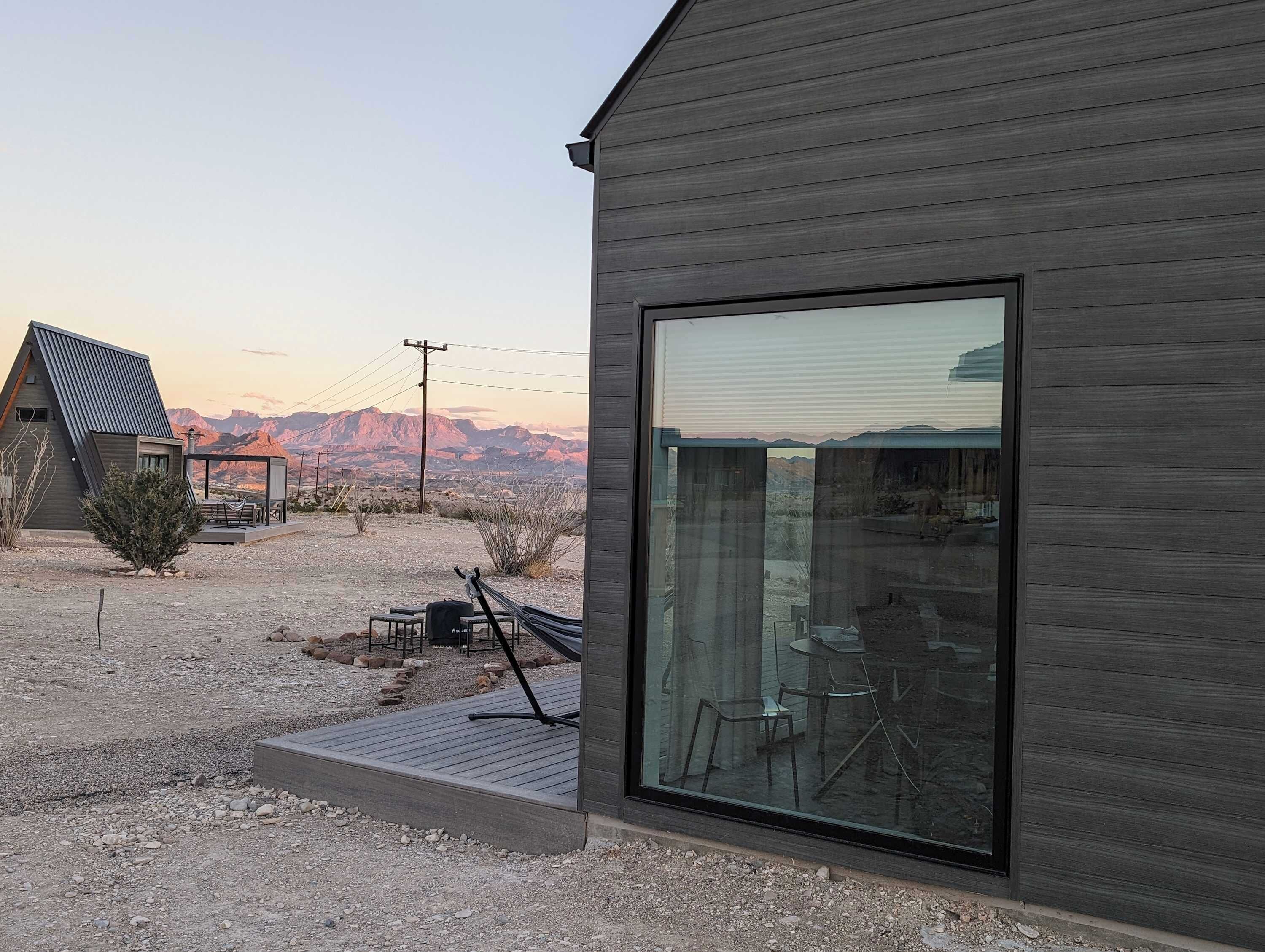 Un bâtiment moderne doté d’une grande baie vitrée, d’un patio avec des meubles d’extérieur et offrant une vue sur les montagnes en arrière-plan.