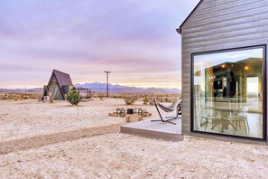 A modern building with a large glass window, a hammock, and a small table with chairs in a desert setting. - Stardust Luxury Cottage with loft & a great view (Terlingua)