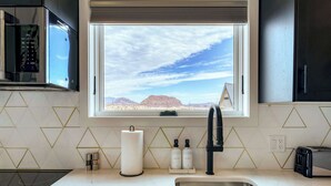 A modern kitchen with a built-in microwave, a stainless steel sink, and a window offering a view of a desert landscape. - Stardust Luxury Cottage with loft & a great view (Terlingua)
