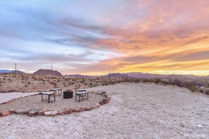 A desert landscape with a sunset, a seating area with tables and chairs, and distant mountains. - Stardust Big Bend Luxury A-Frame#5 great views (Terlingua)