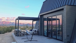 Eine moderne Außenpatio mit Sitzgelegenheiten und einer Hängematte, mit Blick auf eine Wüstenlandschaft und Berge in der Ferne.