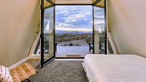 Un dormitori amb un gran fanal, un llit i vista a una terrassa exterior.