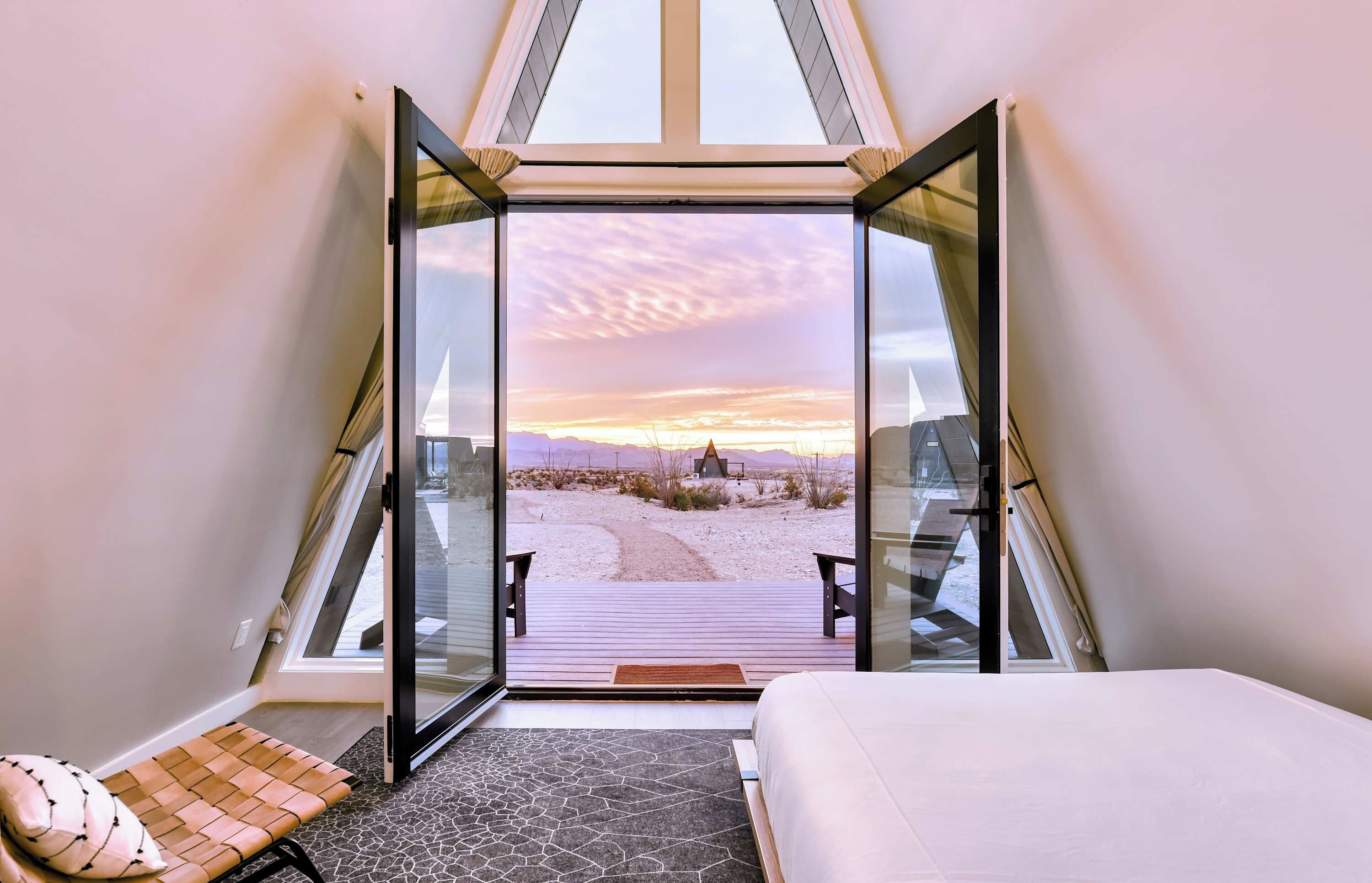 Ein Zimmer mit einem Bett, einer Bank und Blick auf einen Sonnenuntergang über einer Wüstenlandschaft.