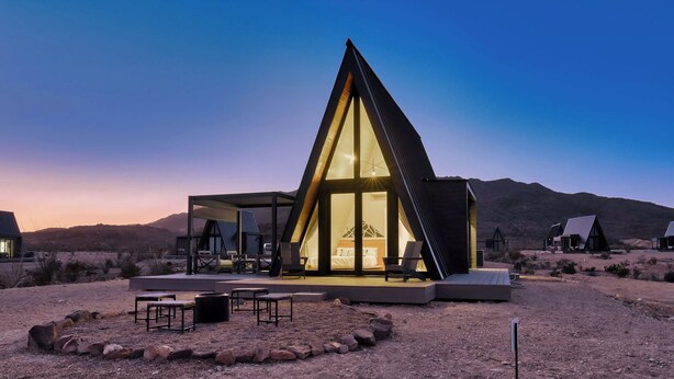 A modern, triangular-shaped building with a glass facade, outdoor seating area, and a view of the surrounding desert landscape. - Stardust Big Bend Luxury A-Frame#1 with a fab view (Terlingua)