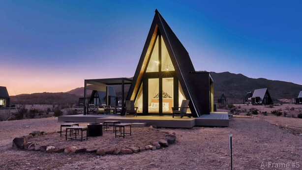 Un bâtiment moderne de forme triangulaire, doté d’une façade en verre, d’un espace extérieur aménagé pour s’asseoir et offrant une vue sur le paysage désertique environnant.