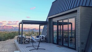 Une terrasse extérieure moderne, dotée d’un espace salon et d’un hamac, offrant une vue sur un paysage désertique et des montagnes.