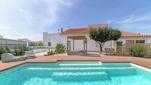 Una piscina con sillas de descanso, una pérgola y una terraza de madera.