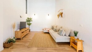 Una sala de estar moderna con techo de madera, un sofá blanco, un televisor sobre un mueble de madera y una alfombra tejida.