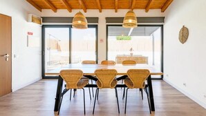 Un comedor con techo de madera, ventanas amplias, sillas de mimbre y una mesa larga.