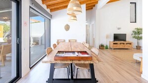 Un comedor moderno con una mesa de madera, sillas de metal negro, una lámpara colgante tejida y un televisor sobre un mueble de madera.