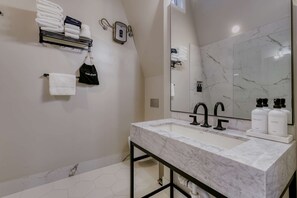 Un baño moderno con lavamanos de mármol, grifos negros y un espejo grande.