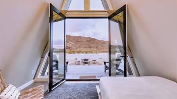 A bedroom with a bed, a chair, and a view of a beach through a glass door.