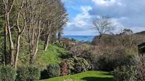 Een weelderig groen landschap met verschillende bomen en struiken, een gazon en een uitzicht op de zee in de verte.