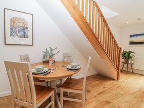 A dining area with a round wooden table, four chairs, a vase with greenery, and a staircase with wooden railings.