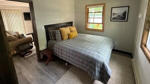 A bedroom with a bed, a window, a chair, and a small stool.