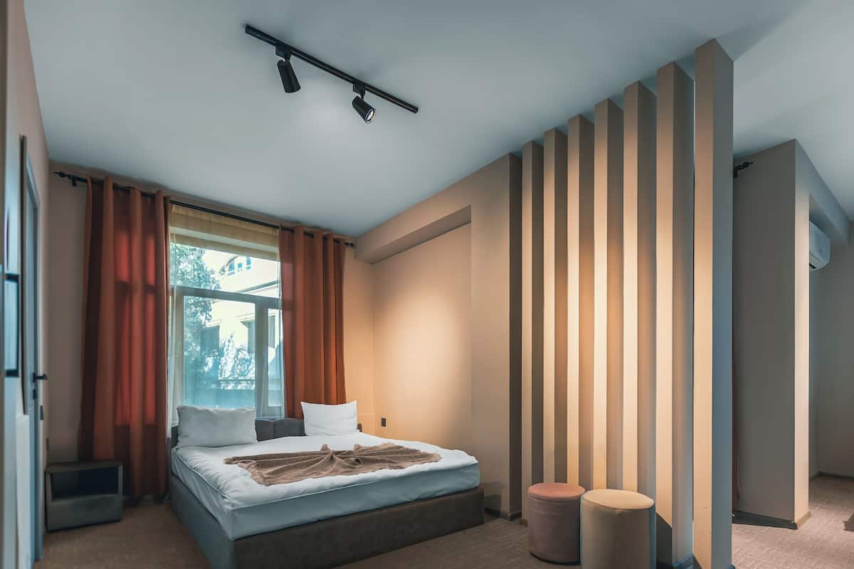 Une chambre moderne avec un grand lit, deux tables de chevet, une fenêtre avec des rideaux et un système d’éclairage intégré au plafond.