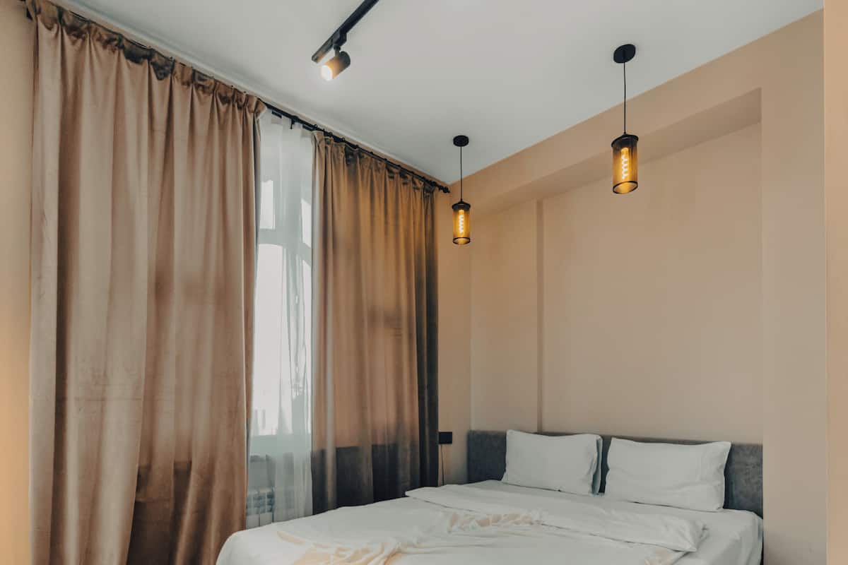 Une chambre avec un grand lit, une fenêtre avec des rideaux et deux lampes suspendues.