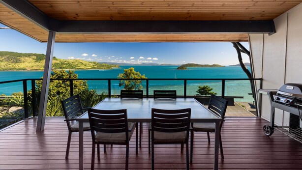A covered outdoor dining area with a view of the sea and hills.