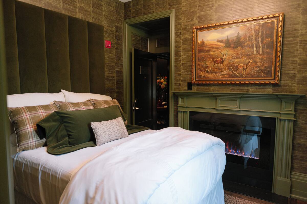 A hotel room with a bed, a fireplace, and a painting on the wall.