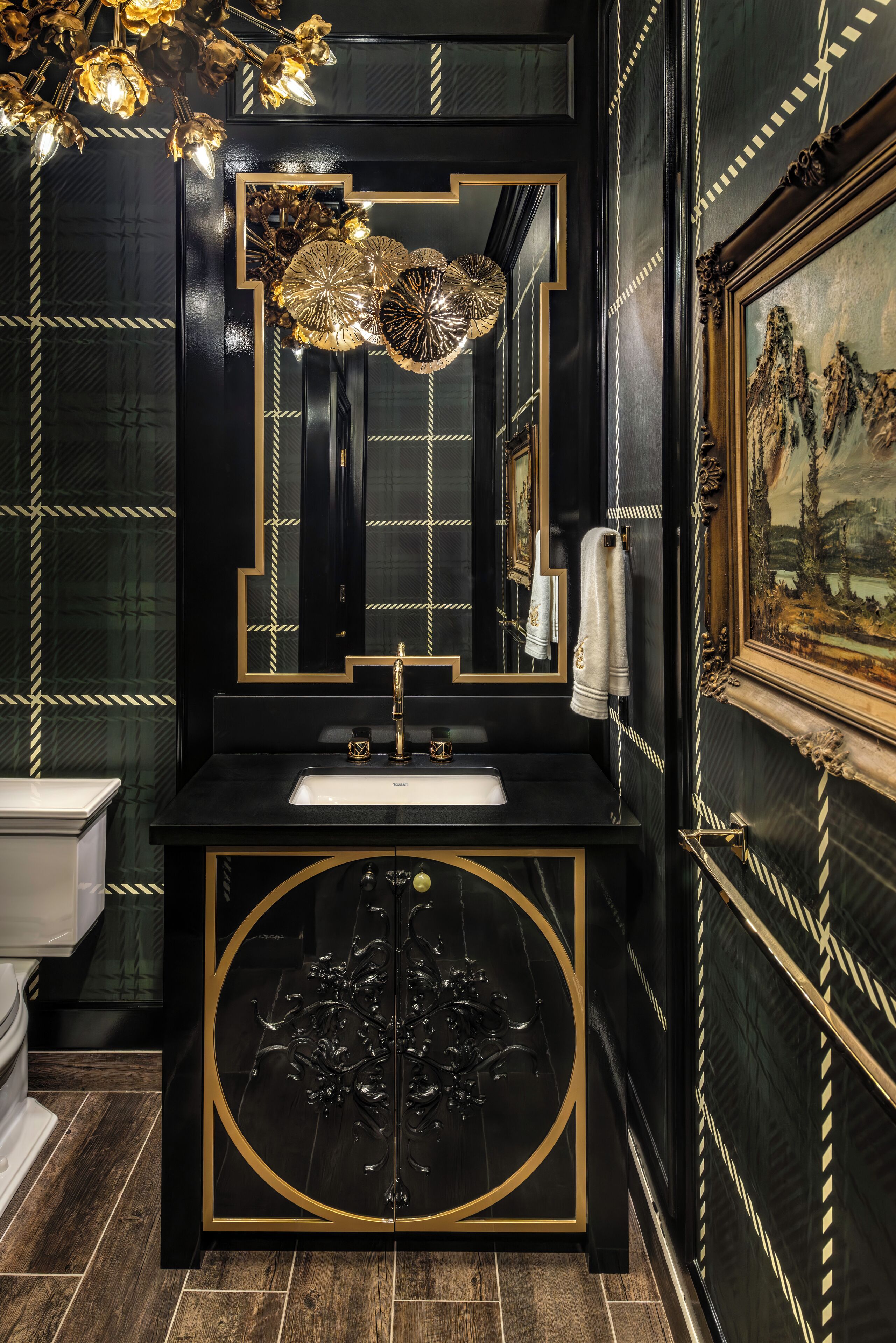 Un baño lujoso con tocador negro y dorado, un espejo grande y una lámpara decorativa.