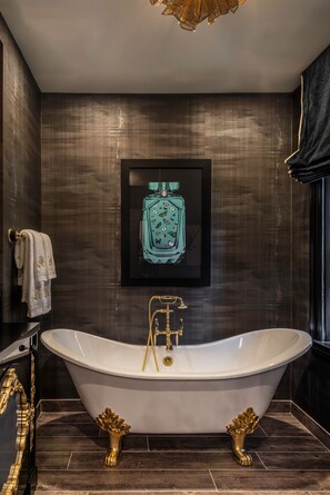 A luxurious bathroom with a freestanding bathtub, dark wood paneling, and a framed perfume bottle artwork.