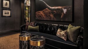 A dark-themed lounge area with a plush sofa, decorative pillows, and a large framed artwork of a horned animal. - The Scotsman Hotel (Niagara-on-the-Lake)