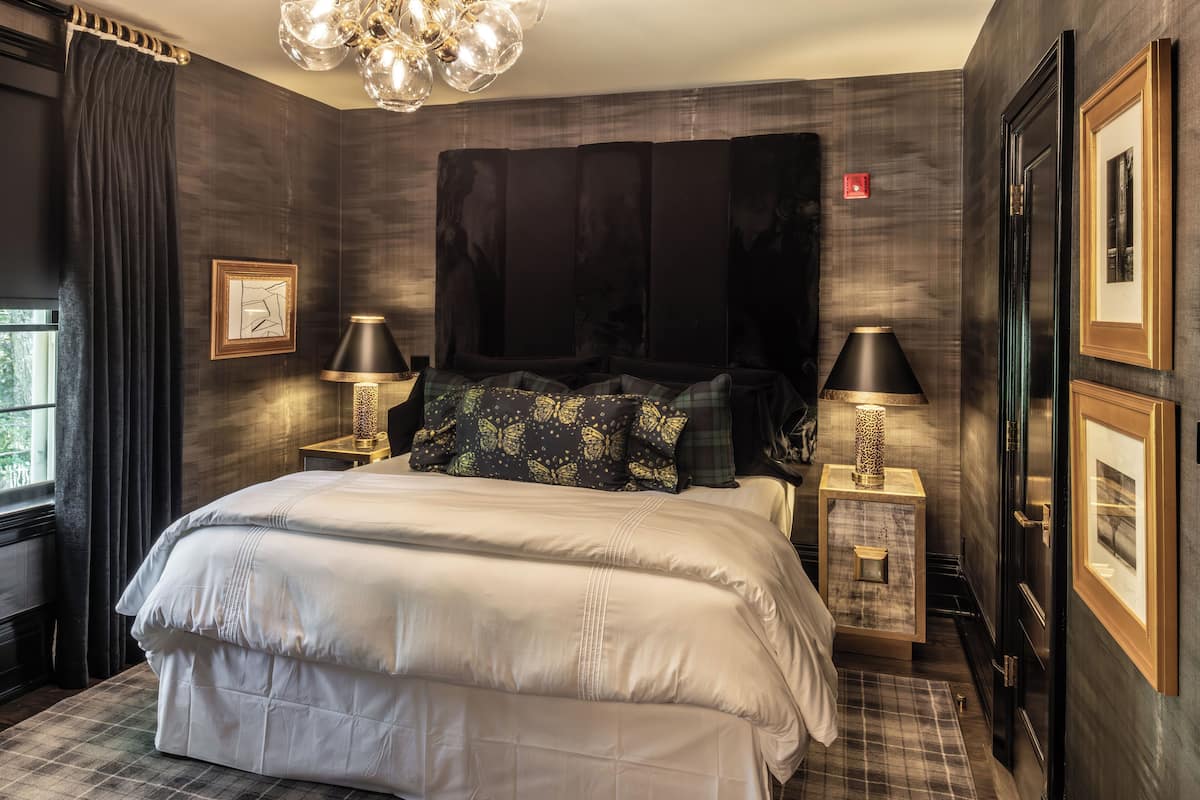 A bedroom with a large bed, two bedside tables with lamps, a dark headboard, and framed pictures on the walls.