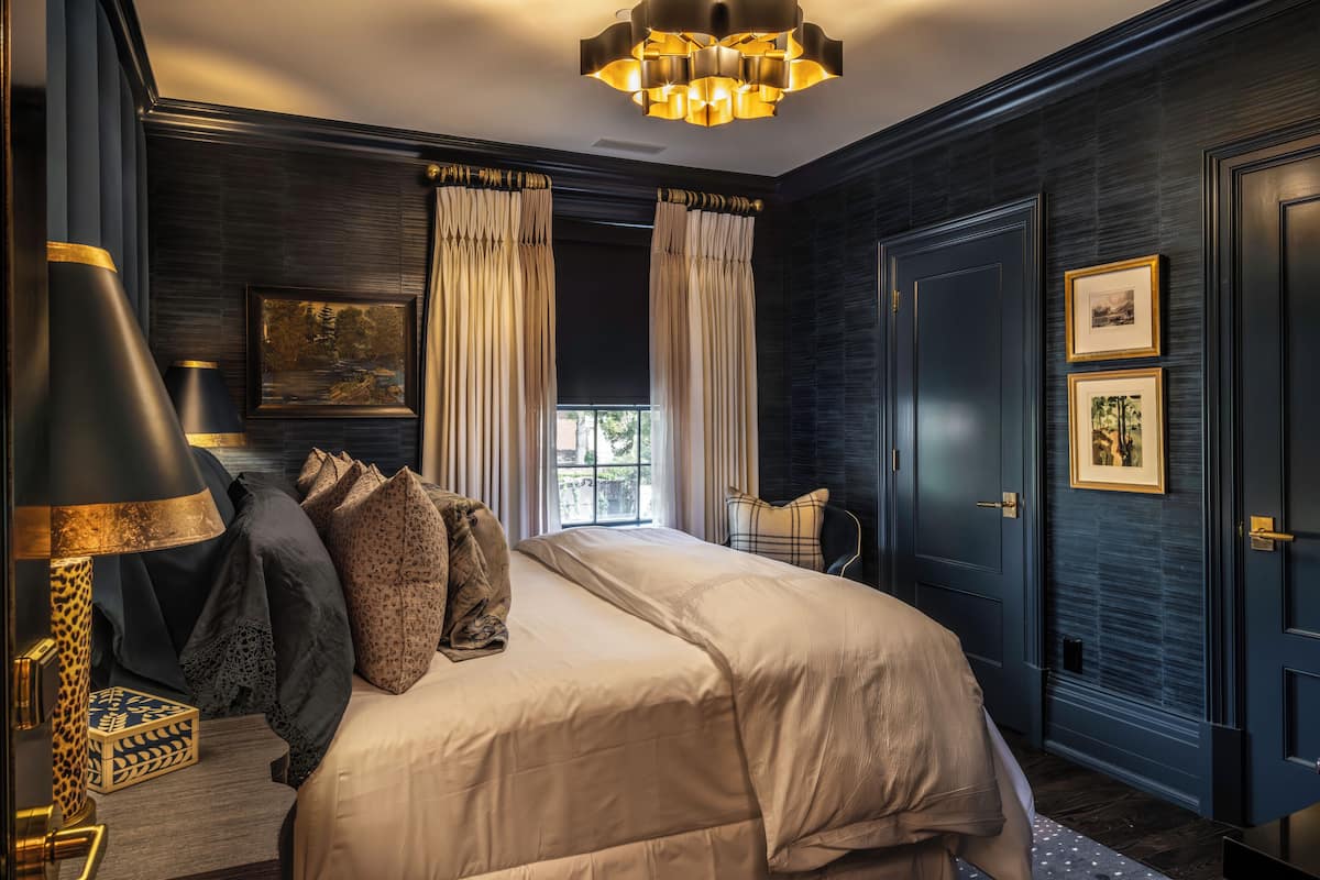 A bedroom with a large bed, dark walls, and a chandelier.