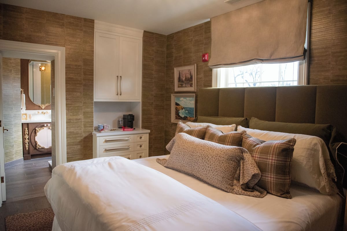 A bedroom with a large bed, a dresser, a vanity with a mirror, and a window with curtains.