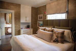 A bedroom with a large bed, a dresser, a vanity with a mirror, and a window with curtains.