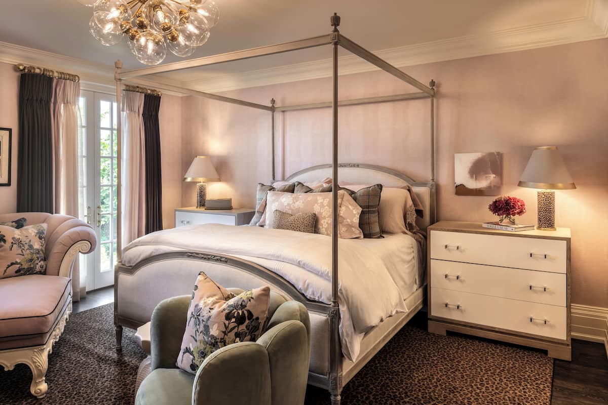 A four-poster bed with a nightstand and a dresser, a chaise lounge, and a chandelier.