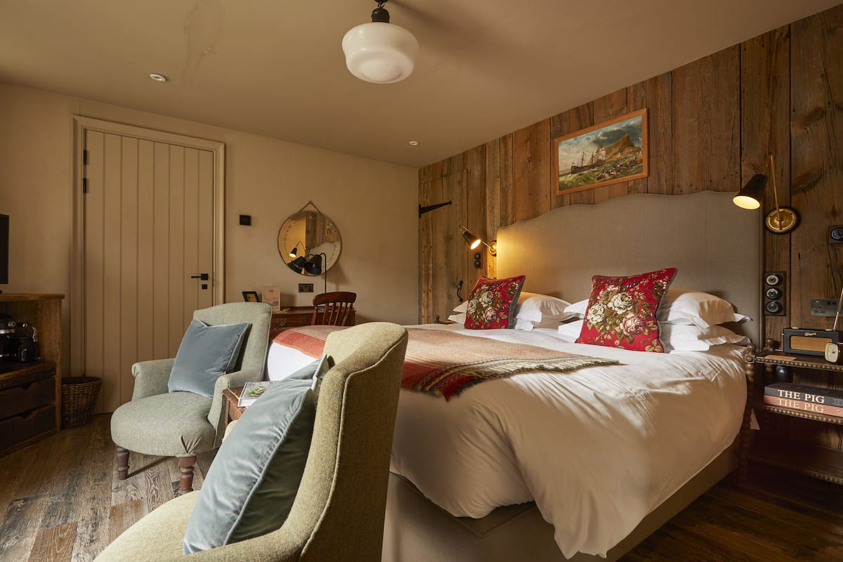 A bedroom with a large bed, a chair, a desk, and a wooden wall panel.