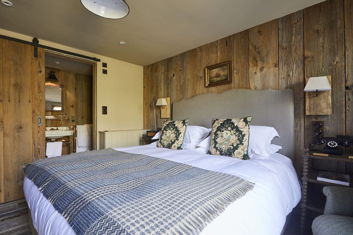 A hotel room with a large bed, wooden panel walls, a bathroom with a sink and mirror, and a nightstand with a lamp.
