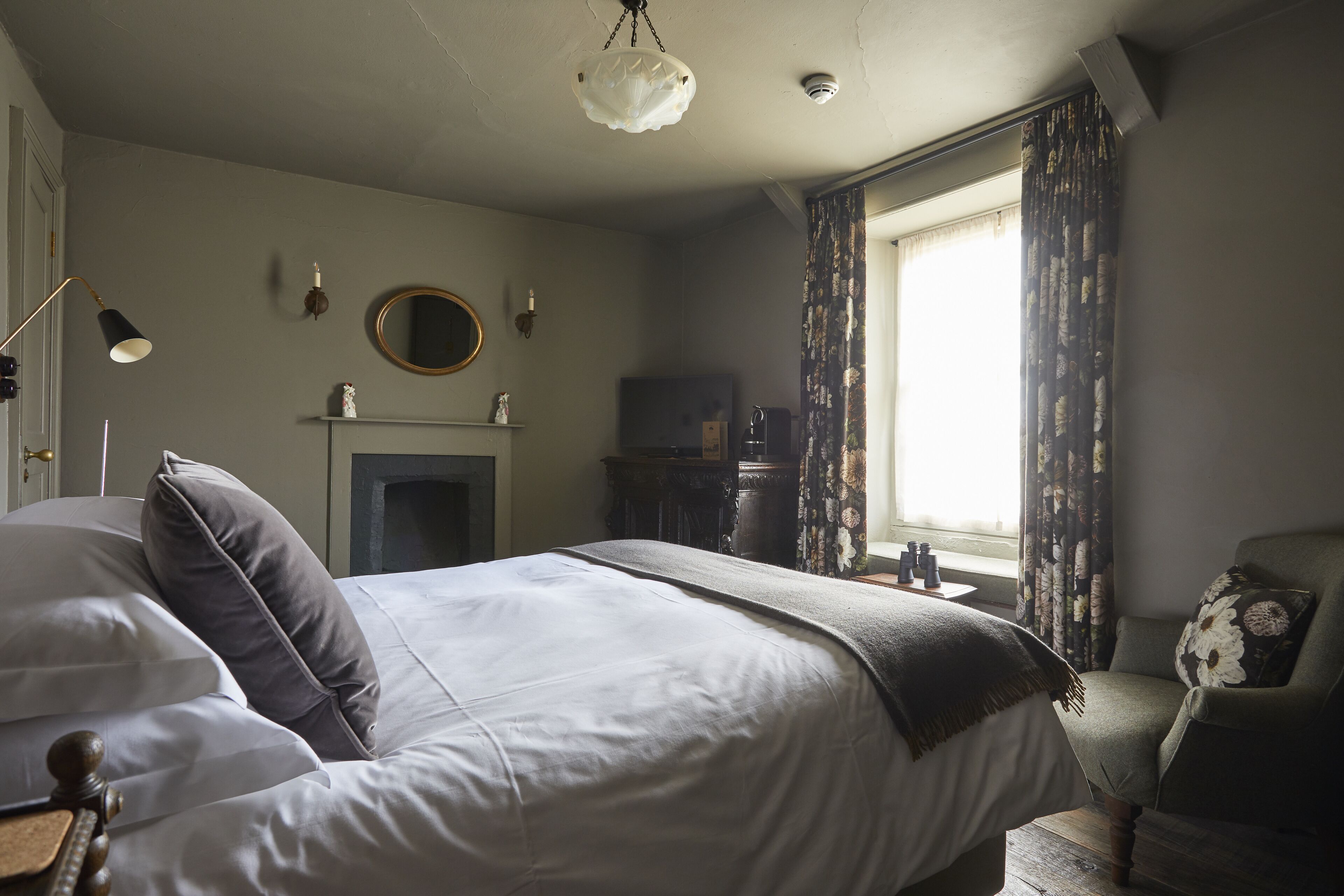 Une chambre à coucher avec un lit, une chaise, une cheminée et une fenêtre avec des rideaux.