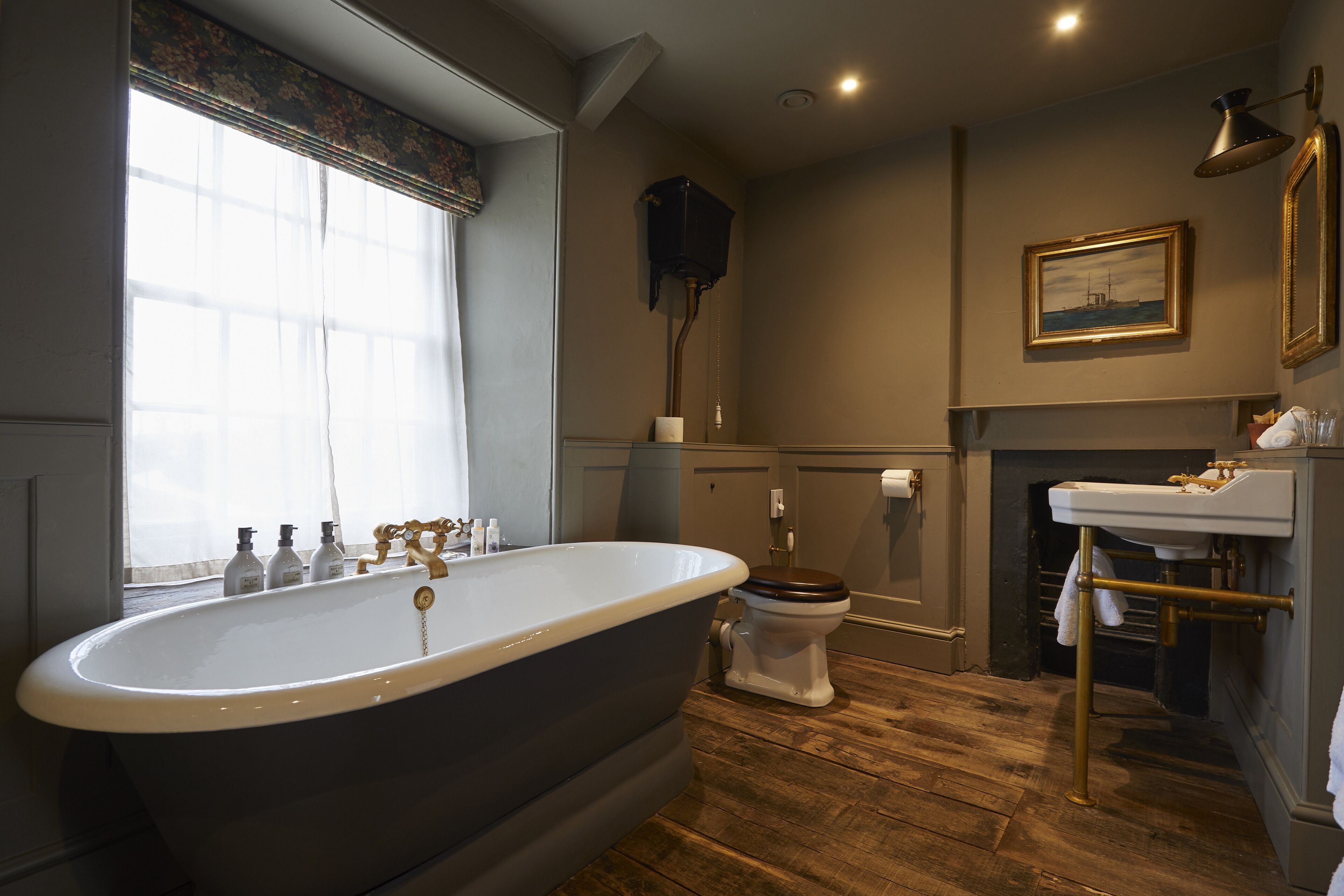 A bathroom with a freestanding bathtub, a toilet, a sink, and a window with curtains.