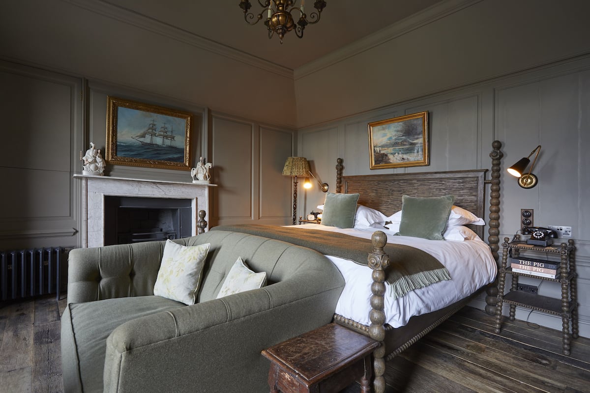 A bedroom with a large bed, a sofa, a fireplace, and two paintings on the walls.