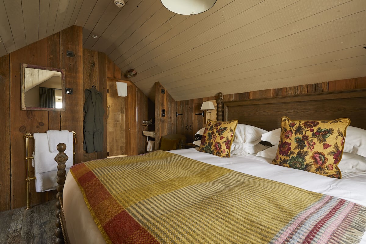 A wooden-paneled bedroom with a large bed, a mirror, and a wooden wardrobe.