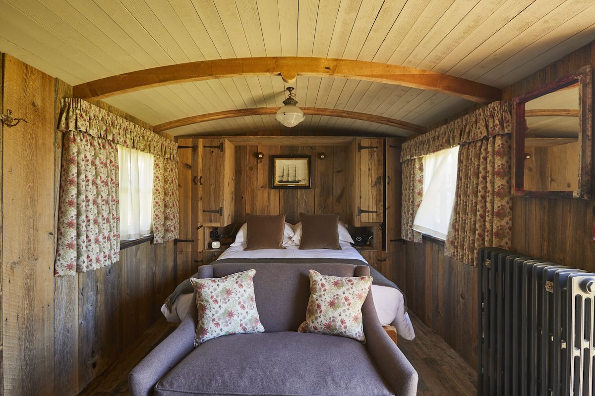 A wooden cabin bedroom with a bed, two pillows, a nightstand, a framed picture, and a radiator.