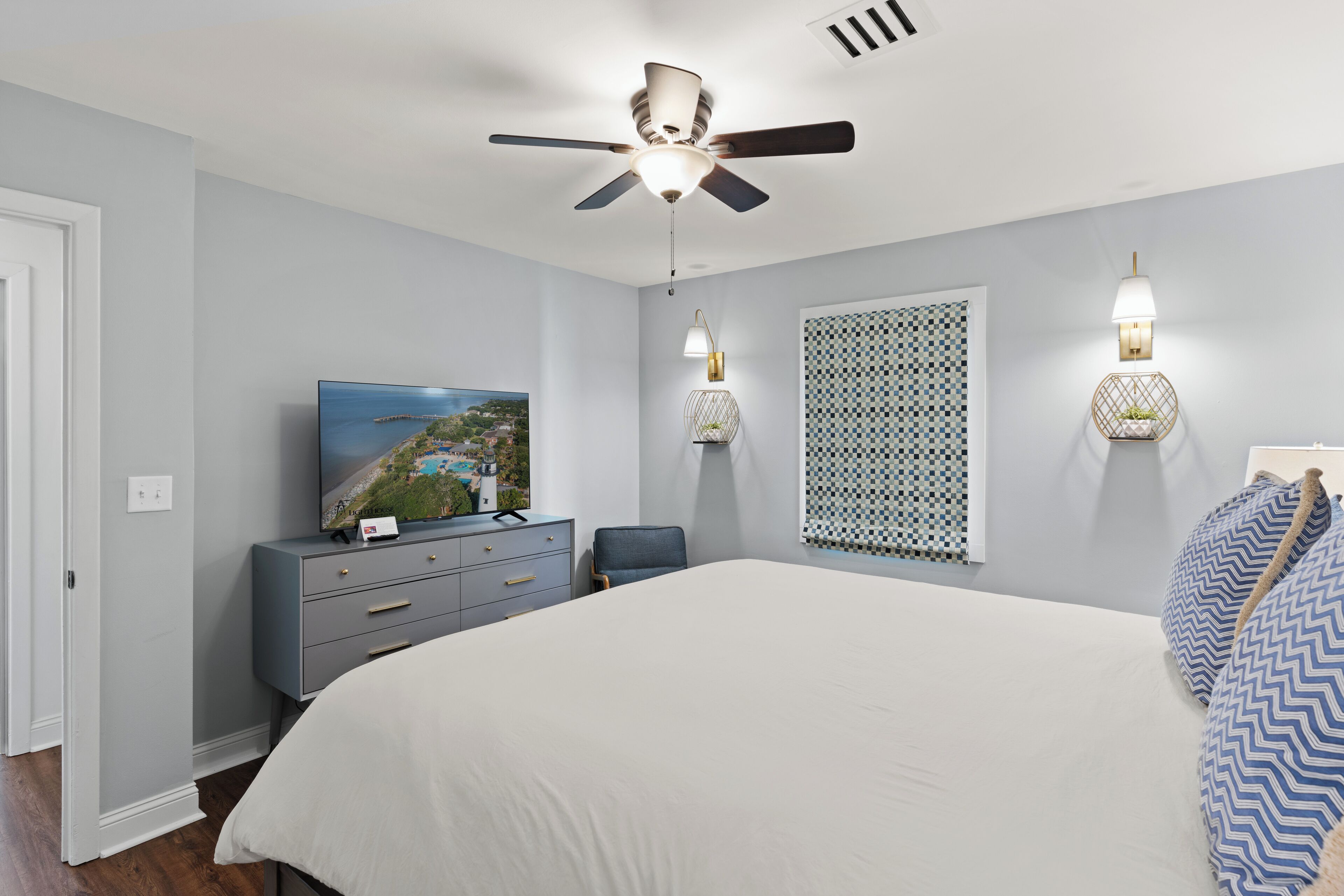A bedroom with a bed, a ceiling fan, a TV, a dresser, and wall sconces.