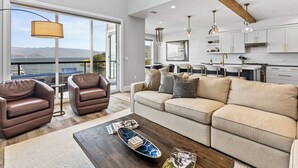 A spacious living room with a large sofa, a coffee table, and a view of the outdoors. - Penthouse w/Private Beach - Seasons at Sandpoint (Sandpoint)