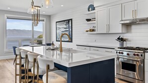 A modern kitchen with a large island, stainless steel appliances, and a view of the sea. - Penthouse w/Private Beach - Seasons at Sandpoint (Sandpoint)